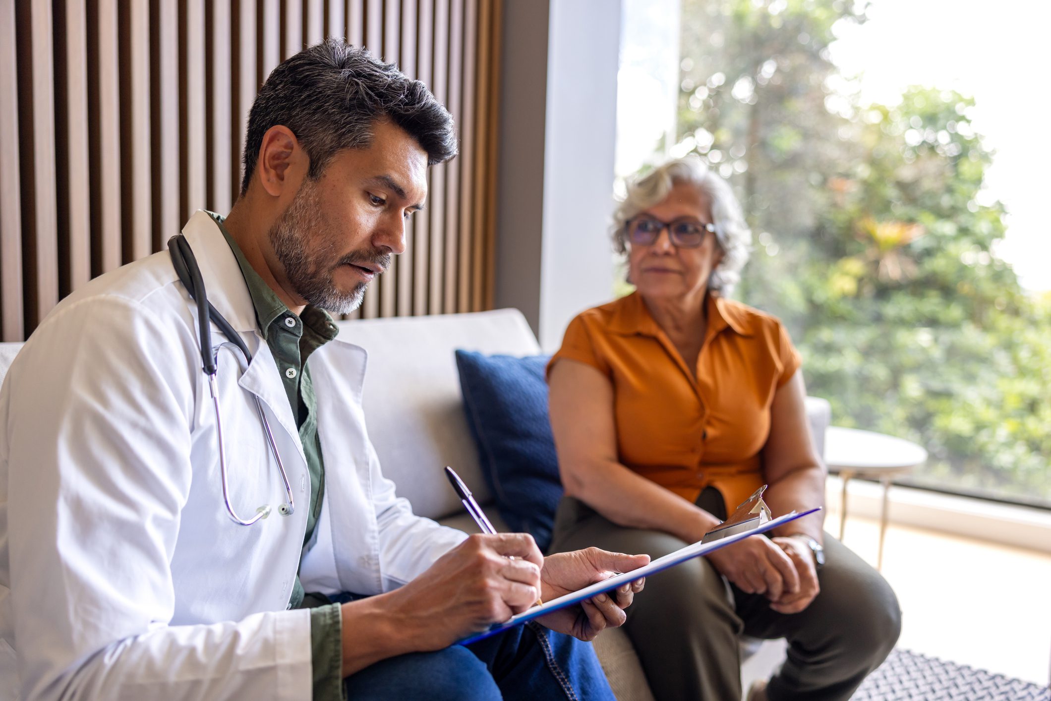 Doctor consulting with senior woman on sofa.